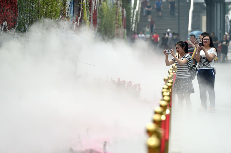 5月19日，在北京西單街頭，幾名行人在噴水霧的花壇旁駐足。