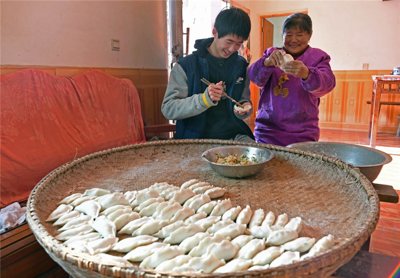 江西鄱陽縣古縣渡鎮張家坽村村民胡桂花（右）和孫子在家里做米粑（1月24日攝）。