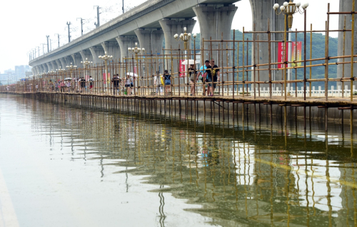 7月12日，行人從武漢湯遜湖橋上的臨時棧橋上走過。受暴雨影響，全長1000多米的武漢湯遜湖橋被猛漲的湖水中斷了橋面交通，至12日積水尚未退去。自7月8日起，為了方便群眾出行，江夏區在湯遜湖橋上開始施工搭建人行棧橋，目前行人可從已經搭建成功的棧橋上步行通過。新華社記者 程敏 攝