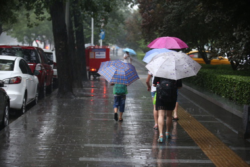 7月20日，行人在北京宣武門西大街上冒雨前行。