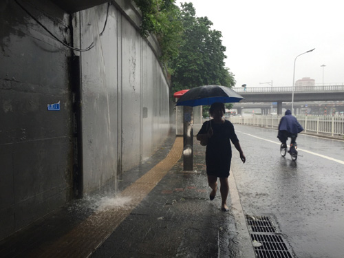 7月20日，行人走過北京蓮花橋橋下的一處排水口，隨著雨量增大此處排水口已經像個“小瀑布”。