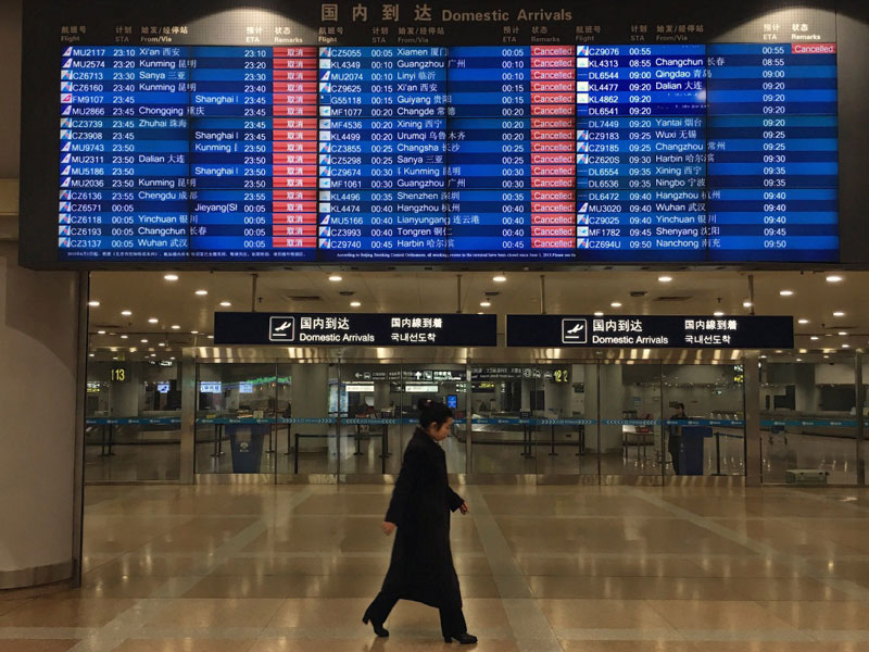 12月20日，在北京首都國際機場T2航站樓，一名工作人員走過顯示航班取消的電子屏幕。