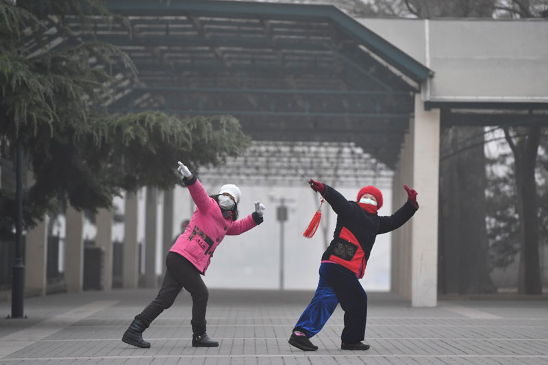 12月21日，兩名市民在霧霾籠罩的陶然亭公園內舞劍晨練。